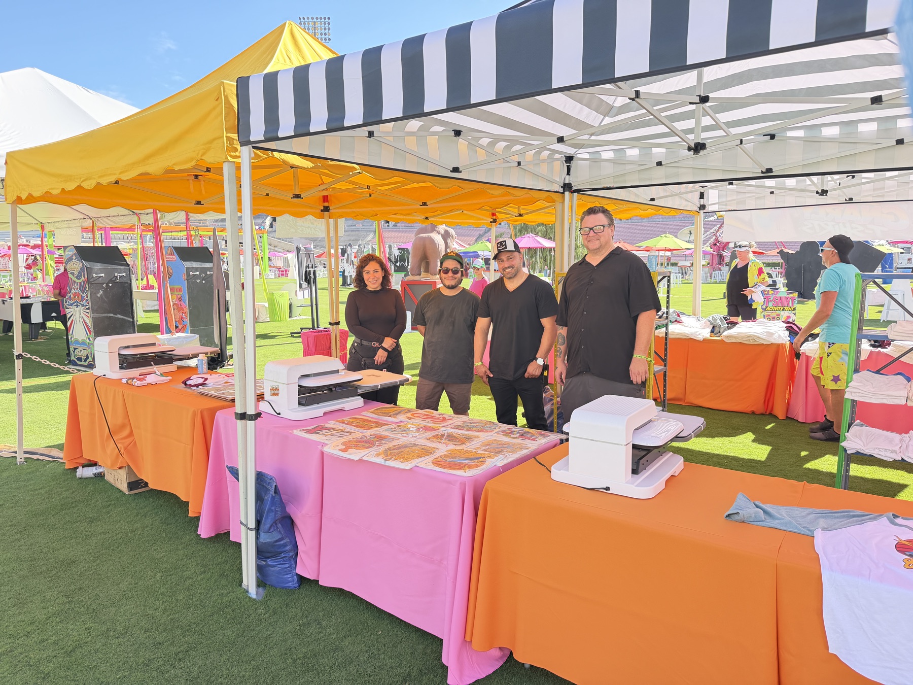 Merch Troop crew beside three live DTF heat press stations on the Rose Bowl field in Pasadena